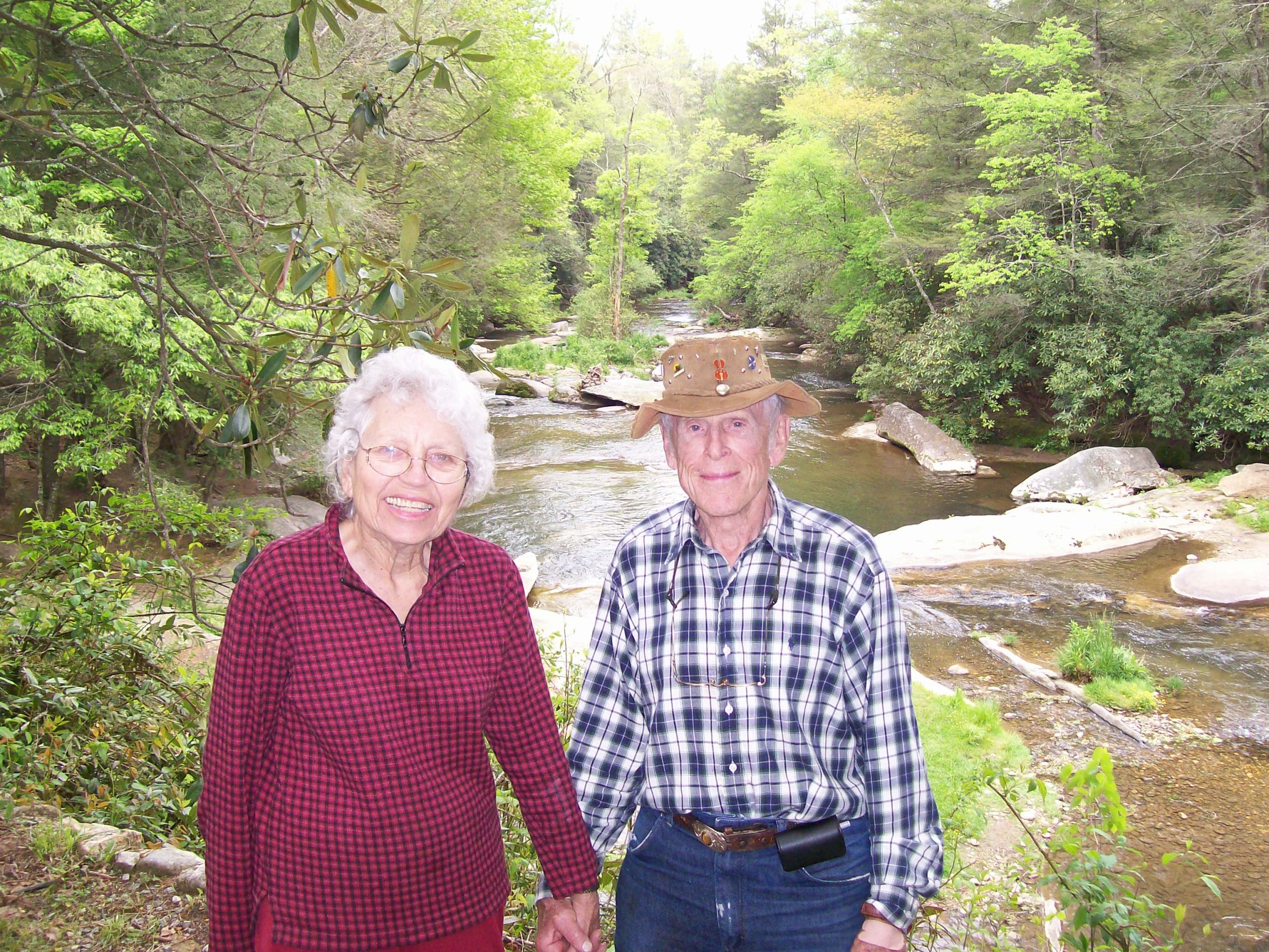 Older woman and man holding hands posing in from of a river.