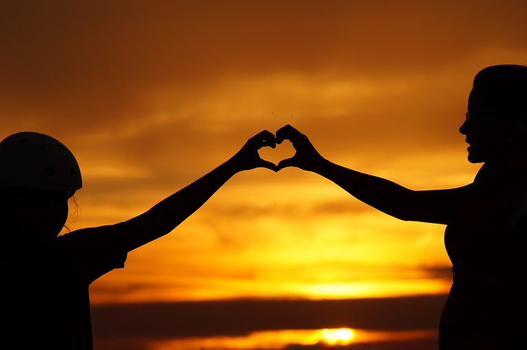 Silhouette of two people forming a heart with their hands.