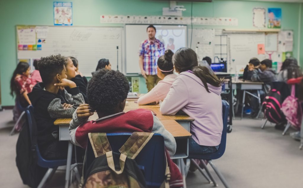 teenagers sitting at desks looking at the teacher standing by the white board.