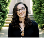 Girl with brown hair and glasses smiling while sitting on steps with greenery in the background.