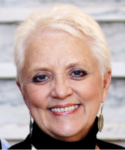 Woman with short white hair smiling in front of a white background.