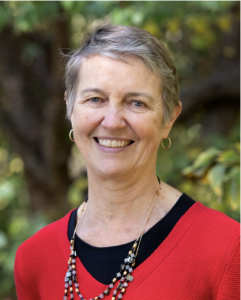 Woman smiling with a red shirt and greenery in the background.